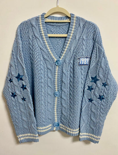 A Sky Blue Taylor Swift inspired cardigan from 1989 Taylor's Version album that features blue stars on the sleeves and 1989 album with seagulls patch on the chest.